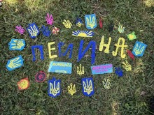 На галявині лежать жовто-блакитні  літери та зібране слово "Перлина", поруч саморобні герби країни та прапор Донеччини.