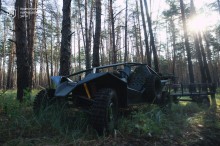 Баггі з причепом стоїть у лісовій зоні. Він використовується для швидкої доставки особового складу, боєкомплекту, продуктів та всього необхідного на передові позиції.