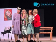 Чотири акторки стоять разом на театральній сцені в обіймах, виконуючи емоційну сцену; позаду видно лавку та фото на білому тлі