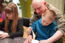 Чоловік допомагає маленькому хлопчику в синьому худі змішувати білу масу в стаканчику.