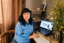 Представниця музею Марина Глушко за столом поруч із ноутбуком, на екрані слайд презентації «Онлайн навчання цифрові навички»