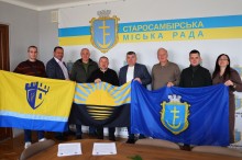 Представники громад тримають прапори Сартанської та Старосамбірської громад та прапор Донецької області
