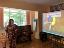 Ведуча заходу стоїть біля увімкненого проєктора, на якому демонструється відеоінструкція з виготовлення оберега