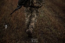 Поле. Розтягуйте оптоволокно, поруч на землі лежить ворожий дрон. Військовий зі зброєю стоїть спиною.