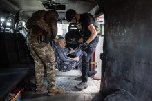Співробітники поліції у повній екіпіровці на ковдрі заносять до броньованого автомобіля літню жінку.