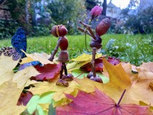 Дитяча поробка, де дві фігурки людей з жолудів та каштанів стоять серед осіннього листя. Одна дарує квітку. Поруч синій метелик