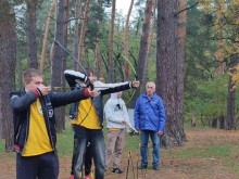 Діти, під наглядом керівника, практикують стрільбу з лука в лісі.