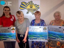 Троє жінок похилого віку одна з них стоїть з палецию та представниця Благодійної організації.  Тримають у руках коробки з картинами по номерам.