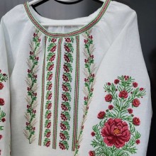 Біла жіноча вишиванка на вішаку, прикрашена яскравим рослинним орнаментом