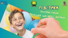 Хлопчик радісно усміхається на фоні кульок. Банер фотовиставки «Усмішка щасливої дитини» з логотипами організаторів.