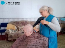 Жінка похилого віку сидить у перукарському кріслі поруч перукар, яка тримає фен у руках та робить укладку.