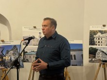 Олександр Шевченко виступає перед мікрофоном на тлі стендів з фотографіями пам'яток архітектури