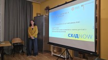 Спікерка виступає з презентацією, на екрані - статистика щодо кількості переселенців