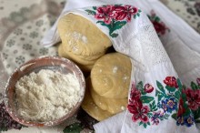 Тісто, прикрите вишитим рушником, та глиняна миска з борошном на столі