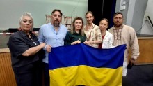 Актори та організатори вистави спільно тримають великий прапор України на сцені біля стільців.