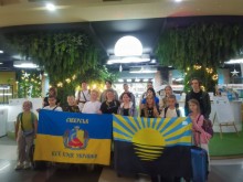 Дівчата та хлопці з Сіверської громади тримають прапори Донеччини та Сіверської громади. Позаду велика біла куля, яка світиться.
