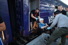 Волонтери допомагають літній жінці спуститися на платформу евакуаційного потяга у Тернополі.