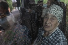 Салон броньованого автомобіля, де сидять літні жінки. Жінка дивиться у вікно, в очах сльози.