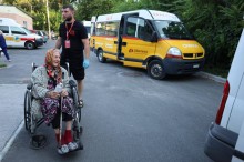 Бабуся на колісному візку в супроводі волонтера поруч з автобусами, якими доставили евакуйованих до місця призначення.