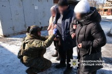 Дві жінки тримають чоловіка під руки, навколішках сидить пармедик, який оглядає чоловіка після обстрілу