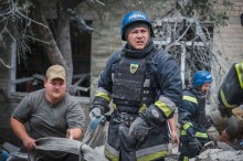 Пожежники в синіх шоломах і спорядженні інтенсивно працюють на місці катастрофи, прибираючи уламки. Їхні обличчя випромінюють зосередженість і рішучість.