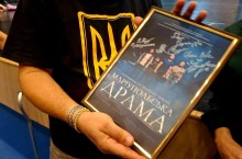 Чоловік у футболці з тризубом тримає в руках підписану акторами рамку з вистави «Маріупольська драма».