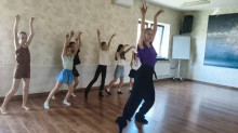 Танцювальний майстер-клас: дівчата та хореограф синхронно повторюють рух із піднятими вгору руками.