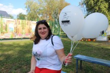 Жінка сидить на лавці у білій сорочці та червоних штанах. Тримає білі кульки з написом "Смолянський куліш"