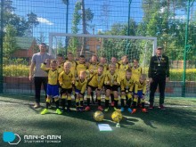 Юні футболісти стоять біля футбольних воріт, по обидва боки тренери, попереду - футбольні м'ячі.