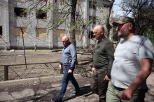 Юрій Винокуров, Вадим Філашкін та Володимир Рибалкін йдуть повз зруйновану окупантами багатоповерхову будівлю.