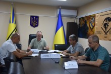 Члени робочої групи з питань евакуації. Сидять за столом, позаду прапори України та Донеччини.
