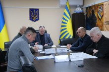 Учасники наради сидять за столом та слухають доповідь