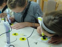 Дві дівчинки малюють 3D-ручками жовті пелюстки соняшників за шаблонами