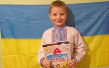 Учасник конкурсу – хлопчик у вишиванці тримає книги українською мовою на фоні прапора України