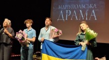 Актори вистави «Маріупольська драма» на сцені тримають прапор України та квіти на тлі екрана з назвою спектаклю.