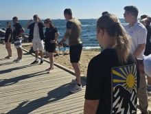 Хлопці та дівчата на березі моря. Молодий чоловік дивиться у бік дівчини та щось показує.