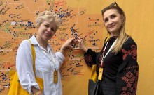 Дві освітянки з Донеччини на тлі карти України під час фестивалю «Вчителі майбутнього – 2025» формують руками серце.