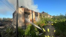 Пожежник гасить одноповерхову будівлю, яка згоріла через російський обстріл.