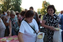 Жінки та чоловіки біля столу, на якому стоїть куліш. Жінка тримає тарілку у руках.