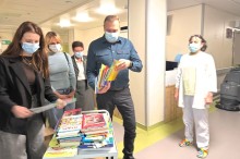 Олександр Шевченко та працівниці лікарні у медичних масках розглядають стос дитячих книжок у коридорі лікарні