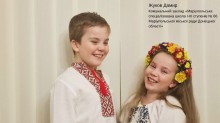 Двоє дітей, хлопчик і дівчинка, одягнені в традиційні вишиті українські сорочки та посміхаються. Дівчинка у яскравому віночку.