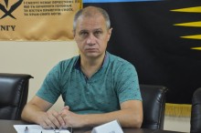 Учасник наради. Уважно дивиться на камеру, позаду прапори військових бригад.