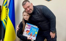 Начальник Великоновосілківської селищної військової адміністрації Сергій Кравченко вручає книжки дівчинці