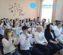 Учасники заходу сидять на стільцях та в руках тримають блакитні та жовті картки.