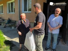 Заступник начальника Часовоярської громади стоїть біля жінки та чоловіка похилого віку. В руках тримає пакет з гуманітарною допомогою. Жінка щось розповідає.