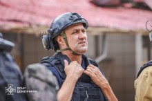 Працівник ДСНС тримає руки біля шиї та відтягує маску від пилу. Лице стурбовано та стомлене.