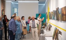 Василь Коренчук розповідає відвідувачам виставки про свої роботи, в залі багато людей