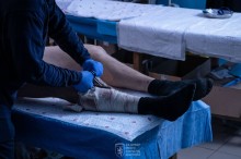 Перев'язка пораненої ноги. Медик обережно знімає просочені кров'ю та забруднені бинти, щоб оглянути рану й накласти нову стерильну пов'язку.