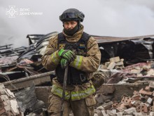 Рятувальник тримає лопату, навкруги зруйнована будівля.