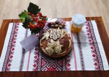 Кругла паляниця з символікою України на рушнику, поруч банка з медом, горіхи та гілочка калини